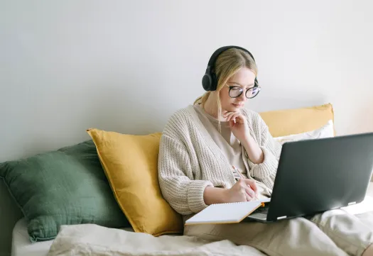 Une étudiante équipée d'un casque audio prend des notes devant son ordinateur en suivant un cours en ligne de la GMS